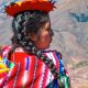A woman in traditional dress looks out over the Andes mountains