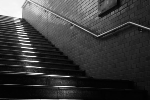 black and white photo of darkened subway stairs leading up to the light