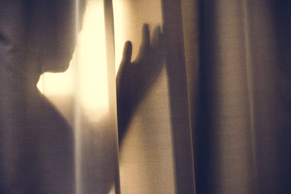 Photo of a woman in the shadows behind a thin drape