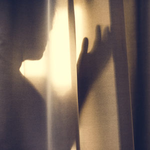 Photo of a woman in the shadows behind a thin drape
