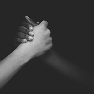 Hands of 2 different people interlocked - one white and one black