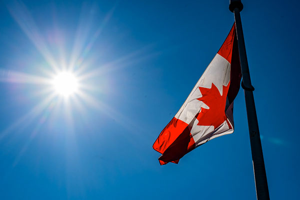 Canadian flag against a deep blue sky and a bright sun