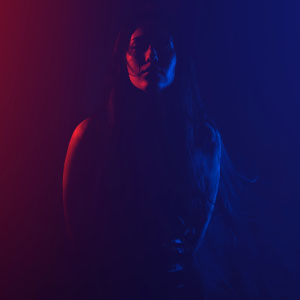 A woman dimly lit by a hazy blue and red wash of light.